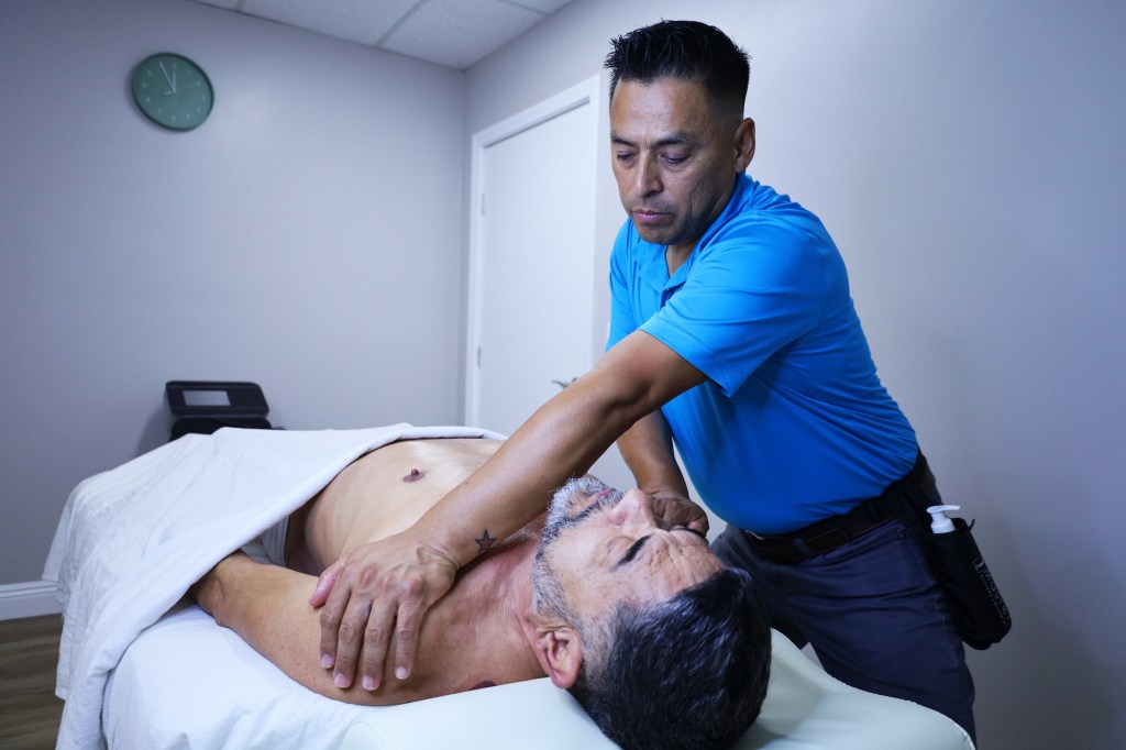 massage therapist places his hands on clients shoulders while client lies on his back in San Diego massage studio